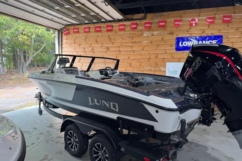 Slide: The Image of 2026 Lund 202 Pro-V GL boat displayed in a showroom with other boats. - 2