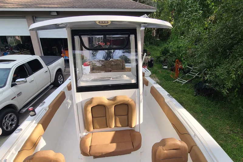 Slide: The Image of 2018 Sea Hunt Gamefish 25 boat with tan seating, parked near a garage and greenery. - 10