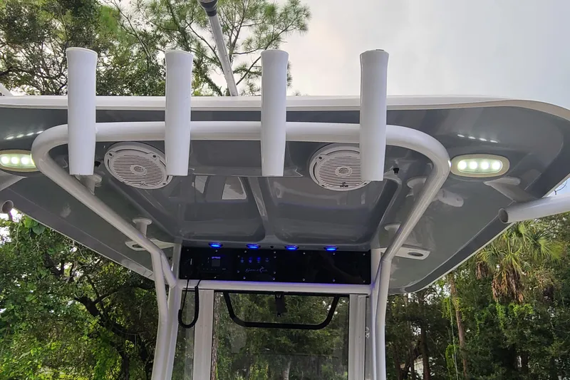 Slide: The Image of 2018 Sea Hunt Gamefish 25 T-top with rod holders and speakers, surrounded by trees. - 27