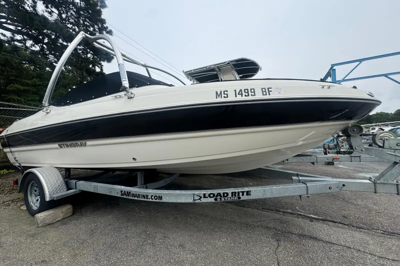 The Image of 2016 Stingray 198 RX boat on trailer, black and white design, parked outdoors. - 1