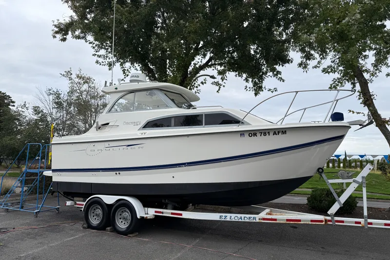 The Image of 2007 Bayliner 246 Discovery boat on trailer, parked outdoors near trees. - 1