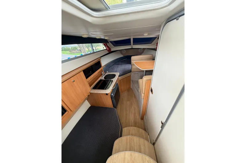 Slide: The Image of 2007 Bayliner 246 Discovery cabin interior with kitchenette, seating, and wood accents. - 15