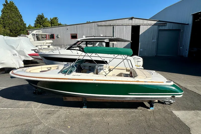 The Image of 2002 Chris-Craft Launch 28 boat with green hull, parked outdoors near a warehouse. - 0