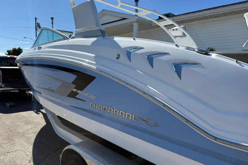 Slide: The Image of 2024 Chaparral 23 SSi OB boat, sleek design, white and blue exterior, parked outdoors. - 26