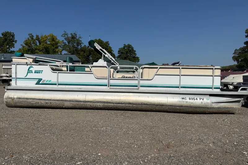 Slide: The Image of 1994 Sun Quest Sea Hunt pontoon boat on gravel, with trees and buildings in the background. - 1