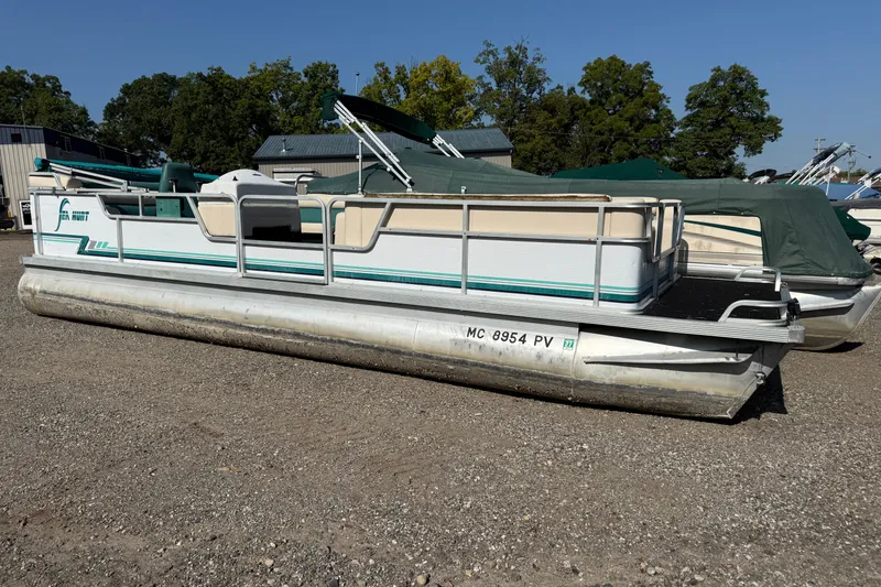 Slide: The Image of 1994 Sun Quest Sea Hunt pontoon boat on gravel lot, surrounded by trees and other boats. - 2