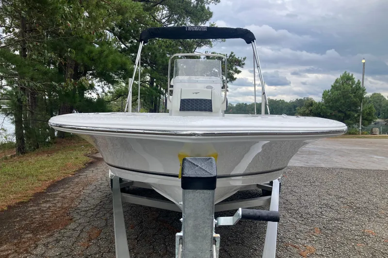 Slide: The Image of 2026 Tidewater 1910 Bay Max boat on trailer, parked near trees under cloudy sky. - 2