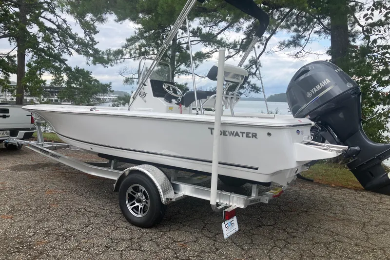 Slide: The Image of 2026 Tidewater 1910 Bay Max boat on trailer, parked near lake with trees in background. - 7