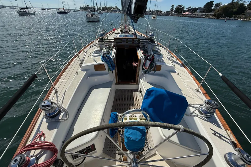 Slide: The Image of 1997 Tartan 3800 sailboat deck with steering wheel, moored in a scenic harbor. - 13