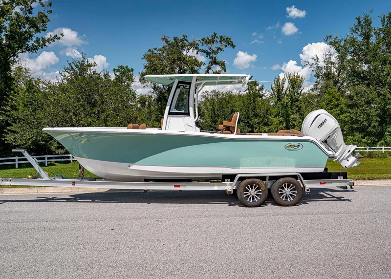 Slide: The Image of 2026 Sea Hunt Ultra 239 boat on trailer, parked on road, with trees in background. - 2
