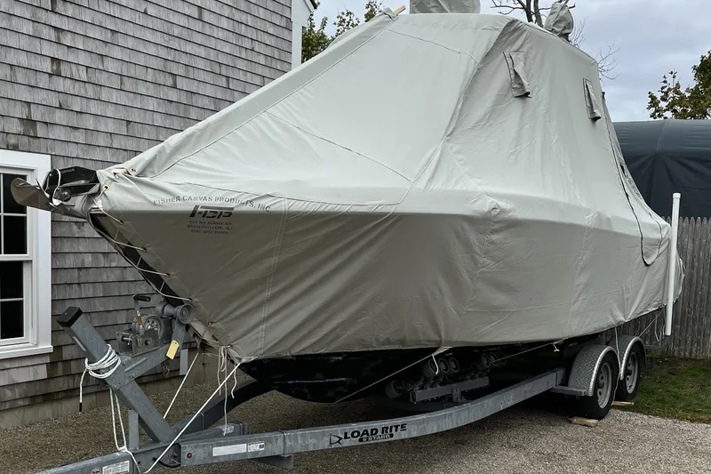 Slide: The Image of 2015 Robalo R242 Center Console boat covered on trailer, parked beside a house. - 56