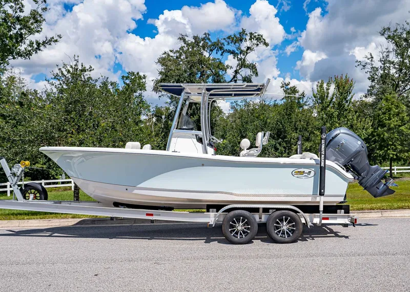 Slide: The Image of 2026 Sea Hunt Ultra 219 boat on trailer, parked on road with trees and cloudy sky. - 2