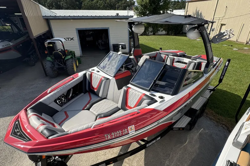 Slide: The Image of 2019 Tigé ZX1 boat with red and gray interior, parked outdoors near a garage. - 12