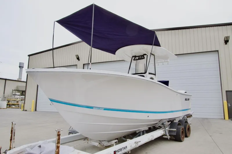 Slide: The Image of 2026 Regulator 25 boat on trailer with canopy, parked outside industrial building. - 2