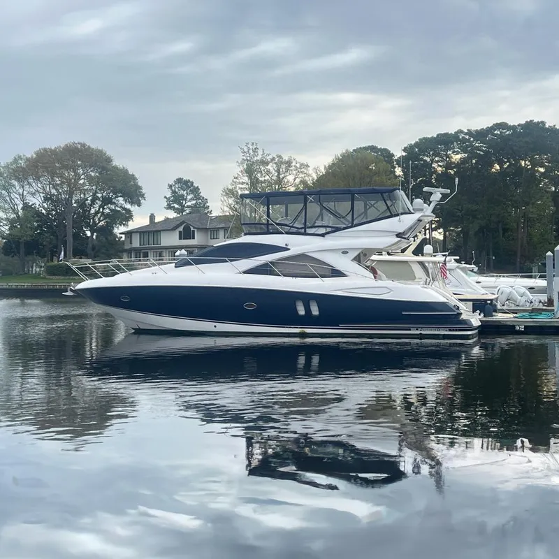 The Image of 2008 Sunseeker Manhattan 50 yacht docked on calm water, surrounded by trees and houses. - 0