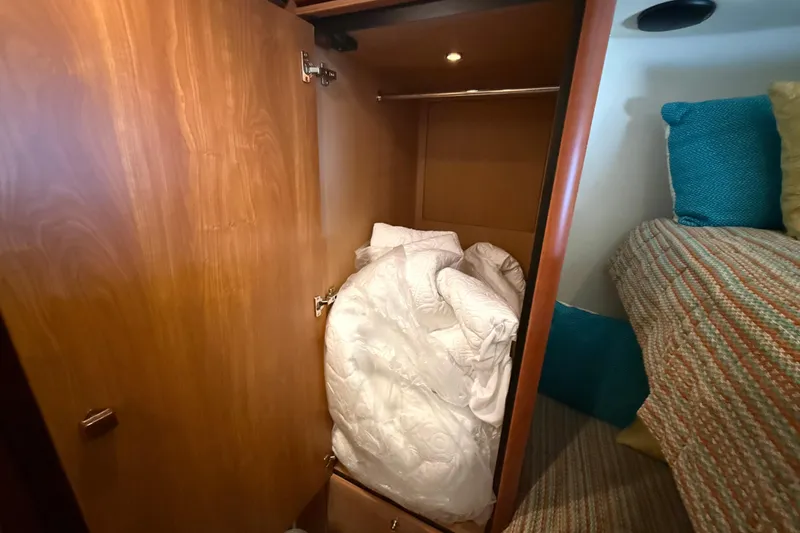 Slide: The Image of Wooden closet with bedding inside, adjacent to a bed with colorful pillows on a Sunseeker Manhattan 50 yacht. - 68