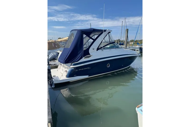 The Image of 2018 Regal 28 Express boat docked in marina, blue canopy, calm water. - 0