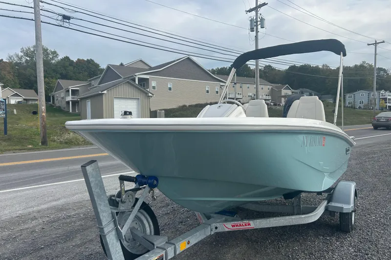 Slide: The Image of 2023 Boston Whaler 130 Super Sport boat on trailer, parked roadside with residential background. - 2