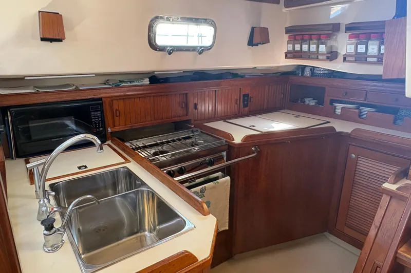 Slide: The Image of 1995 Island Packet 40 yacht kitchen with wooden cabinetry, double sink, stove, and microwave. - 34