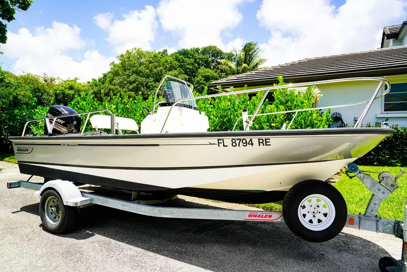 Slide: The Image of 2016 Boston Whaler 170 Montauk boat on trailer, parked in driveway, surrounded by greenery. - 1