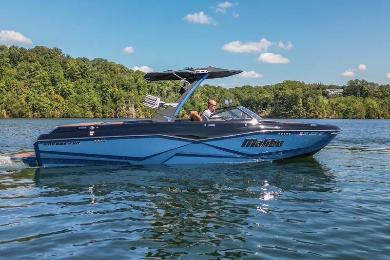 Slide: The Image of 2022 Malibu Wakesetter 25 LSV boat cruising on a scenic lake. - 13