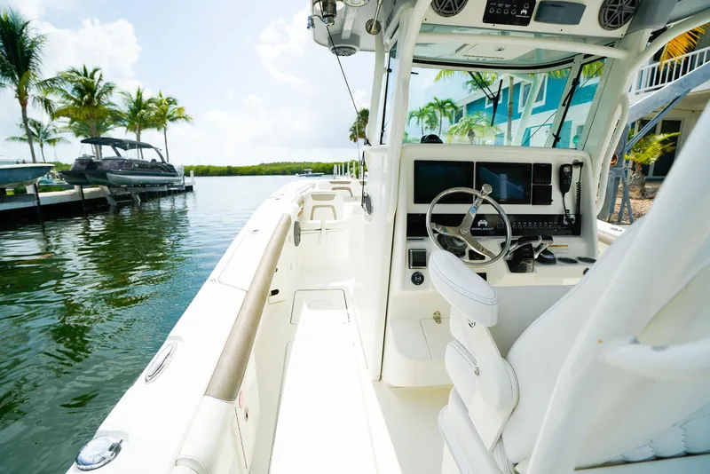 Slide: The Image of 2018 World Cat 320 CC boat interior with steering wheel, docked near palm trees. - 19