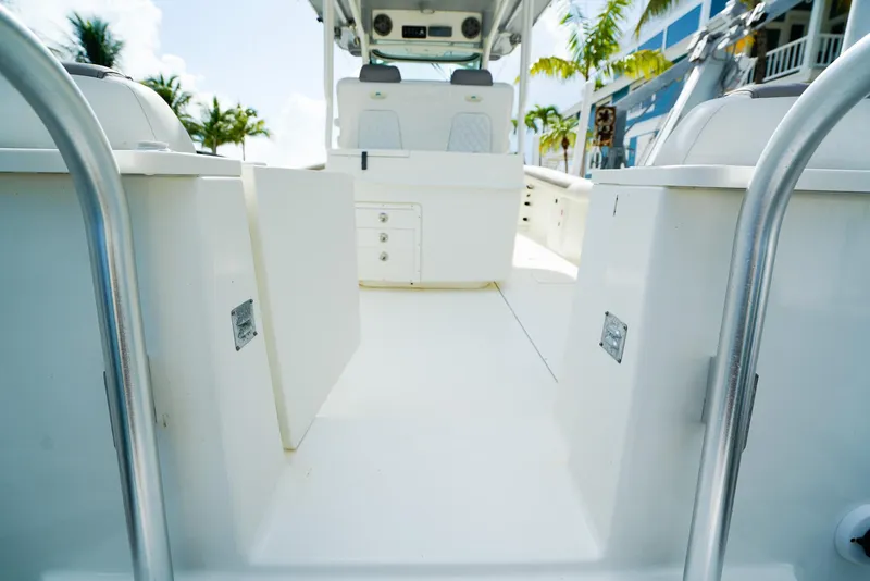 Slide: The Image of 2018 World Cat 320 CC boat interior with white seating and storage, surrounded by palm trees. - 7