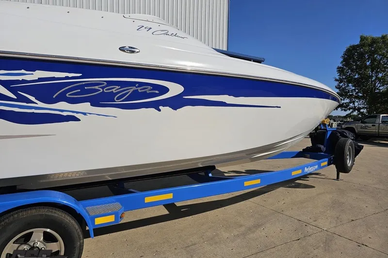 Slide: The Image of 2004 Baja 29 Outlaw boat on blue trailer, parked outdoors under clear sky. - 10
