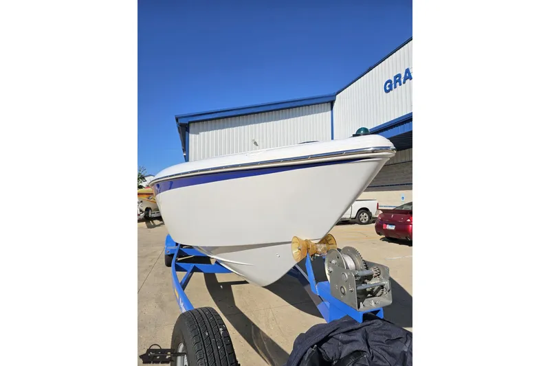 Slide: The Image of 2004 Baja 29 Outlaw boat on trailer, parked outside a building under clear blue sky. - 13