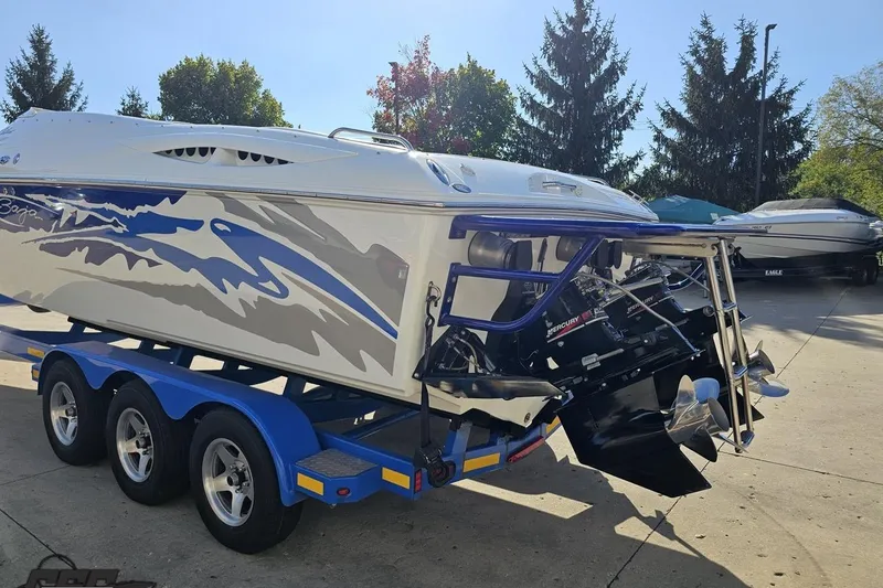 Slide: The Image of 2004 Baja 29 Outlaw speedboat on a blue trailer, parked outdoors. - 27