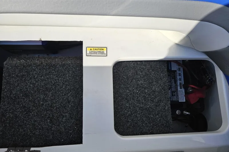 Slide: The Image of 2004 Baja 29 Outlaw battery compartment with caution label and carpeted cover. - 78