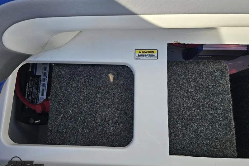 Slide: The Image of 2004 Baja 29 Outlaw battery compartment with caution label and carpeted panels. - 79