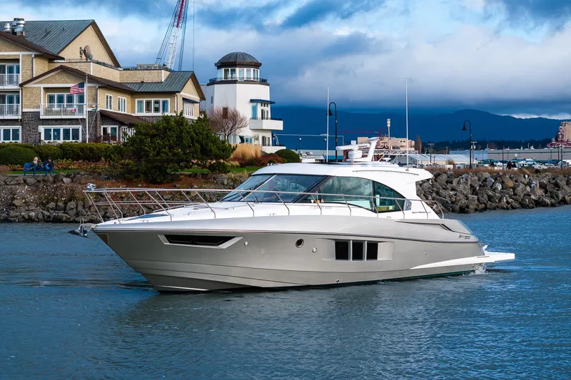 The Image of 2014 Cruisers Yachts 45 Cantius sailing near coastal buildings and rocky shoreline. - 0