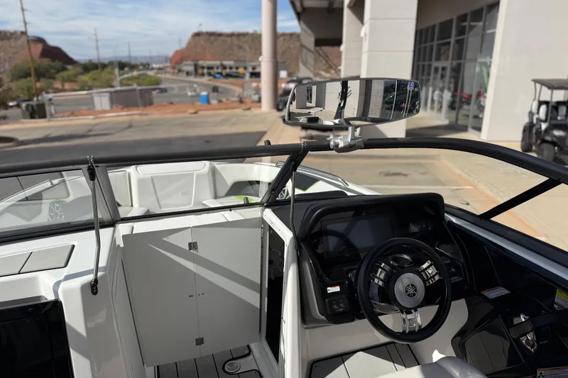 Slide: The Image of 2022 Yamaha Boats 212XD interior with steering wheel and dashboard, parked near dealership. - 59