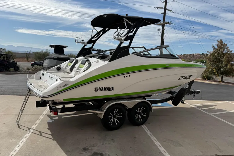 Slide: The Image of 2022 Yamaha Boats 212XD on trailer, white with green accents, parked outdoors. - 7