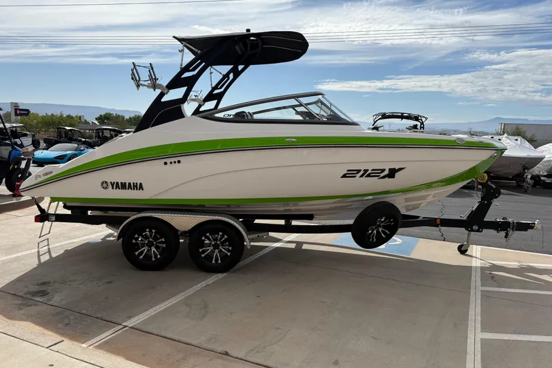 Slide: The Image of 2022 Yamaha Boats 212XD on trailer, white with green accents, parked outdoors. - 8