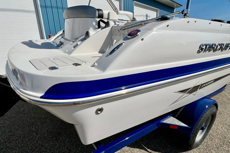 Slide: The Image of 2014 Starcraft 2000 OB Limited boat on trailer, white and blue design, parked outdoors. - 6