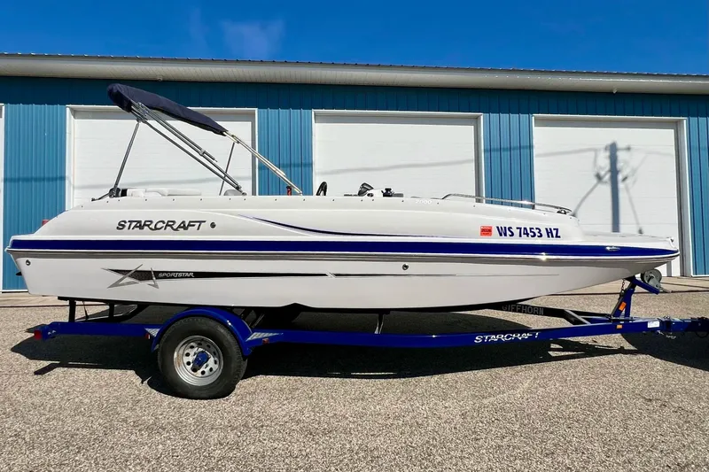 Slide: The Image of 2014 Starcraft 2000 OB Limited boat on trailer, parked outside blue building. - 8