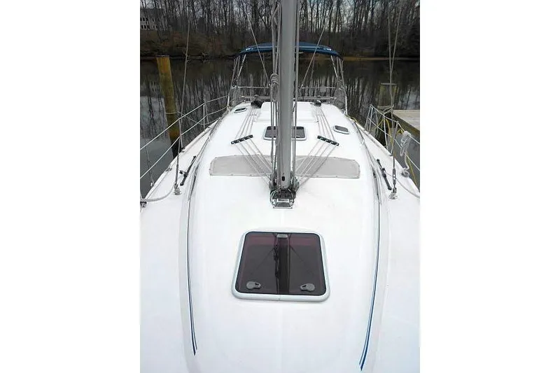 Slide: The Image of 2006 Hunter 38 sailboat deck view with mast and hatch, docked in a wooded area. - 11