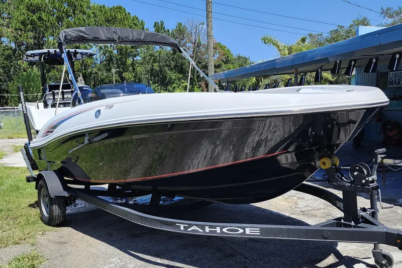 The Image of 2023 Tahoe T18 boat on trailer, parked outdoors near trees and a building. - 0