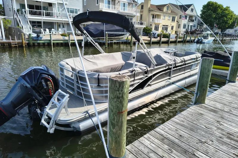 The Image of 2023 Bennington 25 LSRC pontoon boat docked by waterfront homes. - 2