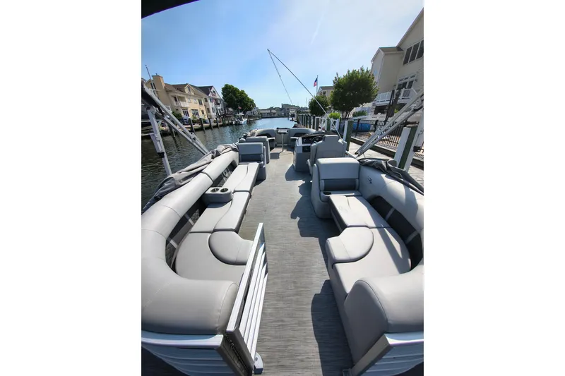 Slide: The Image of 2023 Bennington 25 LSRC pontoon boat with spacious seating, docked by waterfront homes. - 5