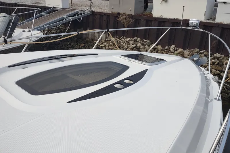 Slide: The Image of 2017 Rinker EX 320 boat bow with sleek design and deck hatch, docked by rocky shore. - 47