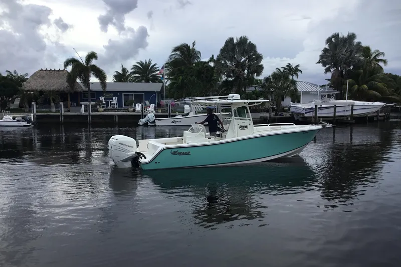 Slide: The Image of 2016 Mako 284 Center Console boat on a calm waterway, surrounded by palm trees. - 75