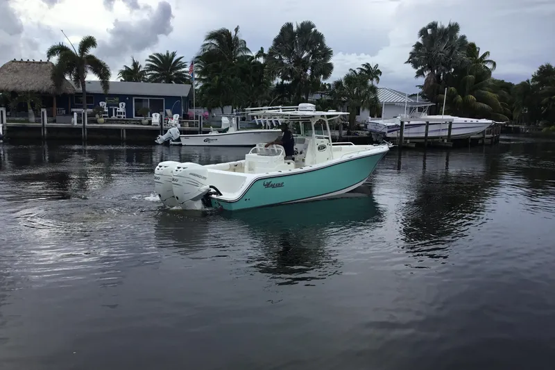 Slide: The Image of 2016 Mako 284 Center Console boat on calm water near a dock with palm trees. - 76