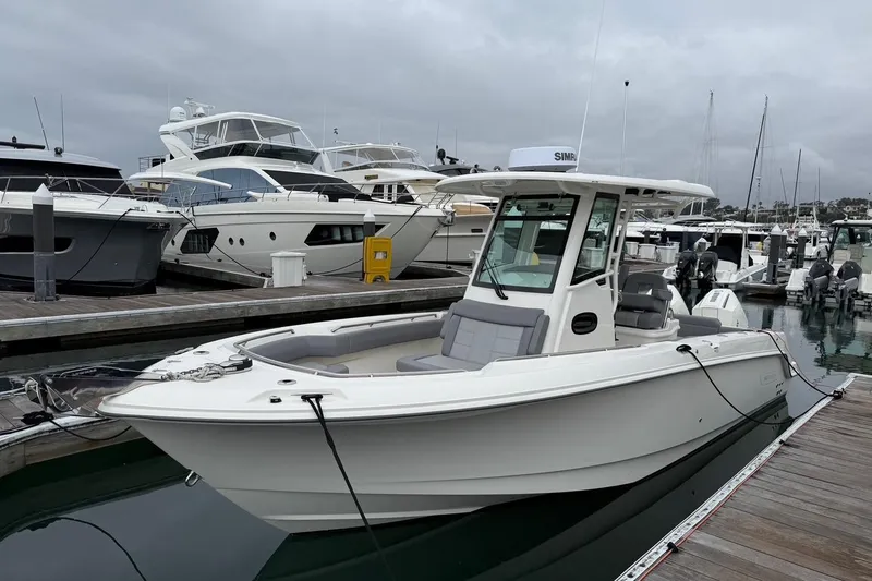 Slide: The Image of 2024 Boston Whaler 250 Outrage boat cruising in a marina with waterfront homes. - 2