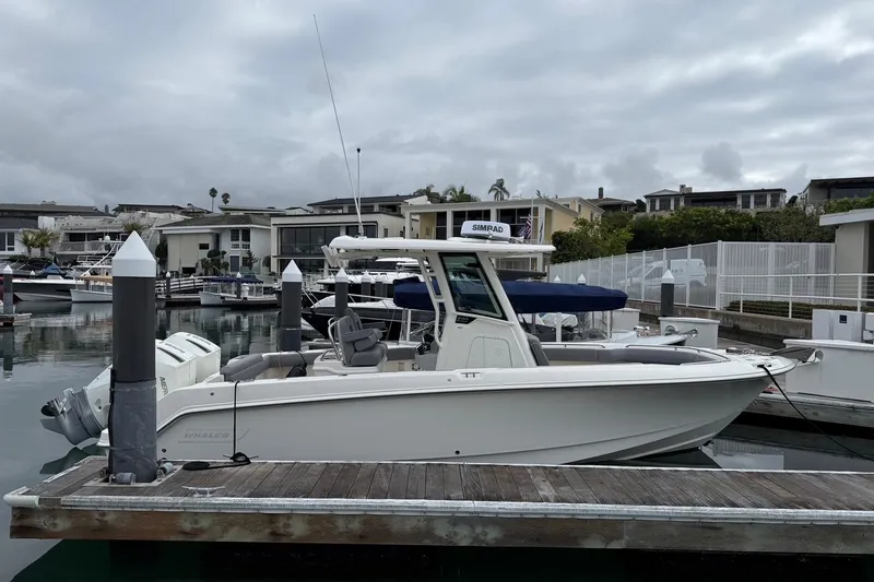 Slide: The Image of 2024 Boston Whaler 250 Outrage boat navigating a marina, showcasing sleek design and powerful engines. - 7