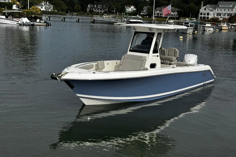 Slide: The Image of 2024 Pursuit S 248 Sport boat on calm water, with houses and docks in the background. - 2
