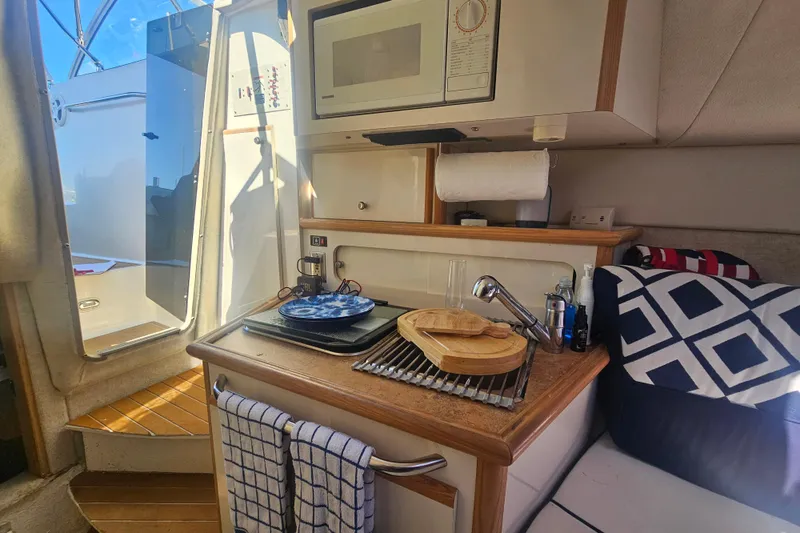 Slide: The Image of 1999 Maxum 2400 SCR boat interior with kitchenette, microwave, and cozy seating area. - 21