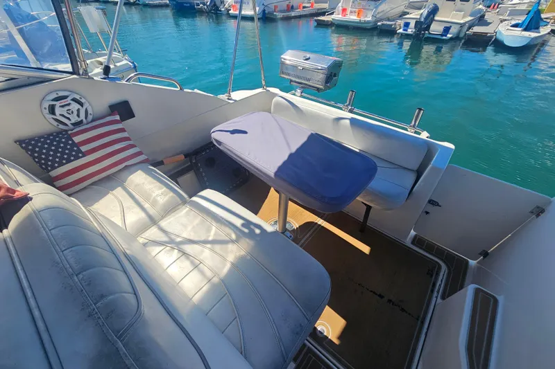 Slide: The Image of 1999 Maxum 2400 SCR boat interior with seating, table, and American flag pillow. - 9